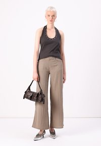 Black halter top with grommet detail, beige wide-leg pants, metallic silver shoes, and small black handbag. Smooth fabric textures noted.