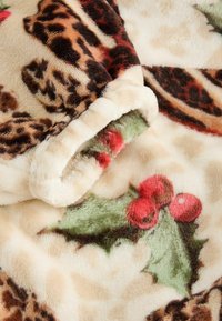 Blød, pelslignende plaid med beige bund, der har leopard- og kristtornmønstre i brune, røde og grønne nuancer. Tekstureret og hyggelig.