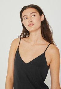 Camisole noire avec des bretelles fines, décolleté en V, fabriquée à partir d'un tissu doux. Présente une coupe ample et une texture lisse, idéale pour superposer.