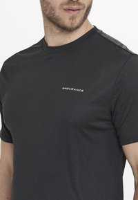 Svart tränings T-shirt med korta ärmar, prydd med en diskret logotyp "ENDURANCE" i vitt, tillverkad av ett mjukt och lätt tyg.