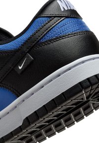 Černé a modré tenisky s texturovaným koženým svrškem, modrými síťovanými akcenty, bílou podrážkou a výrazným logem Nike na boku.