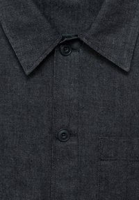 Camicia in denim scuro con colletto a punta, due bottoni neri e tasca applicata sul lato sinistro. Il tessuto presenta una finitura testurizzata.