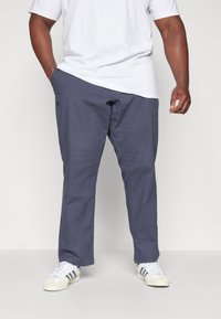 Marineblaue Baumwoll-Chinos mit geradem Bein, Seitentaschen und einer glatten Textur, kombiniert mit weißen Sneakern und einem weißen T-Shirt.