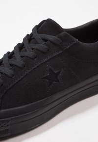 Zapatillas de ante negras con un diseño de corte bajo, que presentan cordones planos negros, un logo de estrella y una suela de goma texturizada.