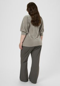 Haut beige à rayures et côtes avec des manches bouffantes, associé à un pantalon large gris foncé sur mesure. Tissu texturé, coupe décontractée.