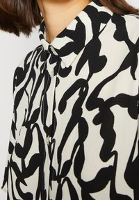 Schwarz-weißes Hemd mit Kragen und abstraktem wirbelndem Muster, leichtem Stoff und sichtbarem Knopfverschluss vorne.