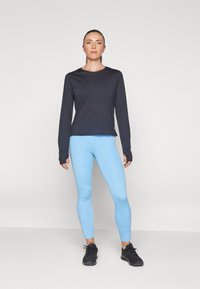 Camisa de manga larga oscura combinada con leggings azul claro, con un diseño ajustado y tela transpirable. Zapatillas deportivas negras completan el conjunto.