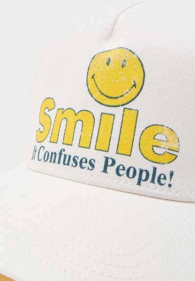 Λευκό καπέλο με κίτρινο χαμογελαστό πρόσωπο και το κείμενο «Smile It Confuses People!» τυπωμένο στο μπροστινό πάνελ.