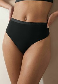 Culotte haute noire en matière lisse et extensible, dotée d'une ceinture décorative avec un logo discret.