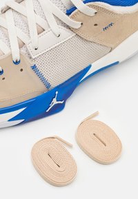Baskets beige et bleues en mesh et daim, avec une semelle en caoutchouc blanche et deux lacets beiges placés à côté.