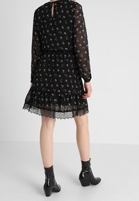 Svart klänning med blommönster, lång ärm och spetsdetaljer, nyckelhålsrygg, lager av volanger nertill, tillsammans med svarta ankelstövlar.