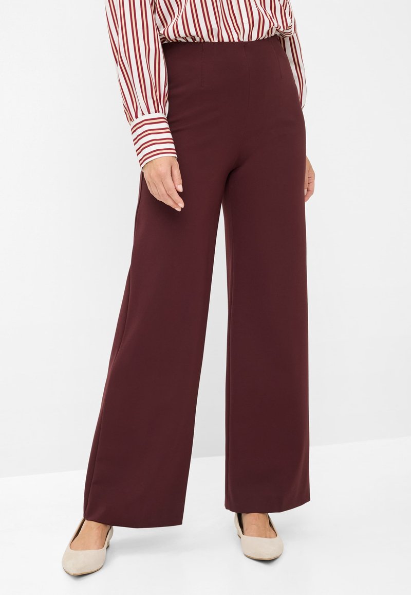 Pantaloni a gamba larga bordeaux realizzati in tessuto liscio, con vita alta e dettagli in cucitura. Abbinati a una blusa a maniche lunghe a righe e ballerine.
