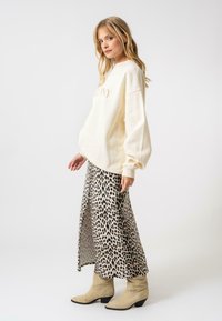 Sweat-shirt crème avec le texte "Harmony", associé à une jupe mi-longue à imprimé léopard et des bottines beiges. Textures lisses et coupe décontractée.