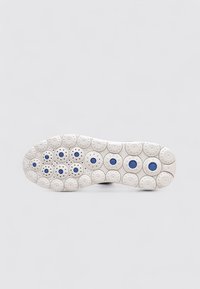 Semelle de sneaker blanche avec des motifs circulaires, accentués de bleu au centre. Texture lisse et design symétrique tout au long.