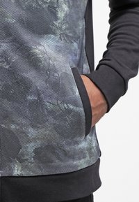 Sudadera con capucha con un frontal texturizado de patrón oscuro y mangas y bolsillo en negro sólido. Presenta un corte relajado y bolsillo tipo canguro.