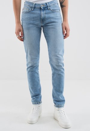 Jeans in denim azzurro chiaro con una vestibilità slim, dotati di cinque tasche e chiusura con bottone. Abbinati a sneakers alte bianche.