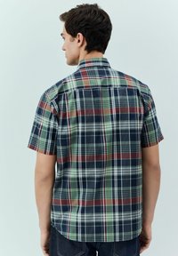 Kurzarm-Hemd aus Karo in dunklem Blau, Grün und Rot. Verfügt über einen Button-Down-Kragen und eine lockere Passform mit Rückenfalten.