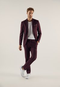 Burgundy suit with slim fit design, featuring a pocket square, paired with a white t-shirt and white sneakers. Smooth fabric texture.