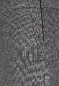 Tessuto grigio a motivi a spina di pesce con una cucitura verticale e una cerniera nascosta. La texture è liscia con un sottile dettaglio tessuto.