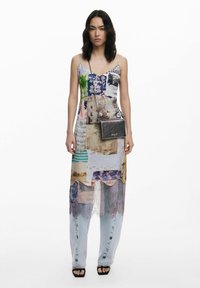 Patchwork maxi dress in mixed textures and colors, featuring a v-neck, layered design, and sheer accents, paired with dark crossbody bag.