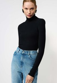 Top negru cu guler înalt, cu dungi și mâneci lungi, asortat cu blugi din denim bleu deschis, cu talie înaltă, evidențiați de un nasture metalic.