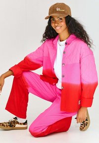 Różowo-czerwony gradientowy pikowany kurtka, dopasowane spodnie i trampki w panterkę. Brązowa czapka z napisem "miłość i inne kolory".