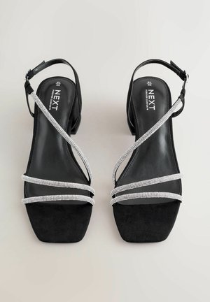 Melni zamša sandales ar kvadrātu purngalu, rotātas ar trim sudraba samta joslām un potītes siksniņu drošai fiksācijai.