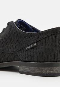 Zapatos negros con un patrón texturizado en zigzag. Fabricados con material transpirable, cuentan con una suela negra de perfil bajo y una etiqueta de logo plateado.