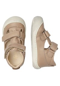 Světlé béžové kožené boty s dvěma nastavitelnými suchými zipy, bílou gumovou podrážkou a prořezávanými bočními detaily. Texturovaná špička a akcenty prošívání.