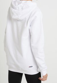 Felpa bianca con cappuccio e cordino, maniche a costine, con un piccolo logo Fila rosso e blu nella parte bassa della schiena. Materiale in misto cotone.