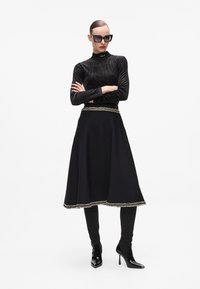 Black textured turtleneck top, black skirt with decorative trim, black fitted leggings, and patent ankle boots with high heels. Black sunglasses.