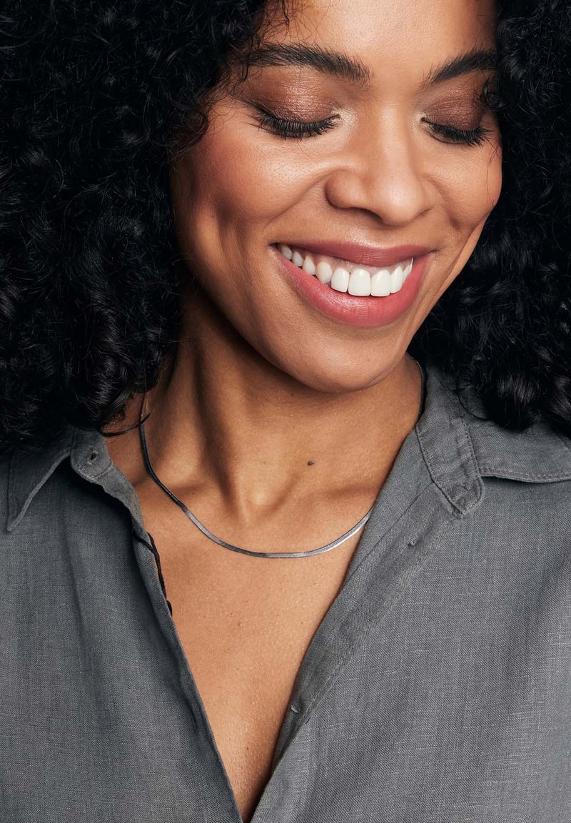 Metalowa naszyjnik o zakrzywionym kształcie, cienki design i gładkie srebrne wykończenie noszony na szarej koszuli z kołnierzykiem, podkreślający linię szyi.