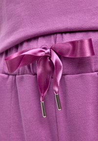 Fioletowy strój sportowy wykonany z teksturowanej tkaniny, z elastycznym pasem oraz satynową wstążką do wiązania z metalowymi zakończeniami. Bez widocznych wzorów ani dodatków.