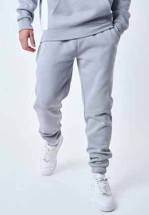 Pantalones de chándal gris claro hechos de una suave mezcla de algodón, con puños elásticos, bolsillos laterales y sutiles acentos texturizados. Combinados con zapatillas blancas.