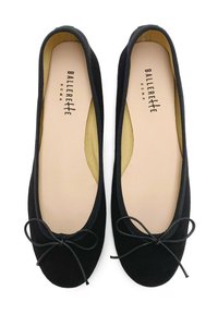 Schwarze Wildleder-Balletschuhe mit abgerundeten Spitzen, elastischem Rand und einer Schleifendekoration auf der Vorderseite. Helle Einlegesohlen sind sichtbar.