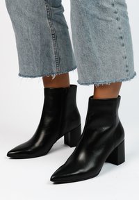 Zwarte leren enkellaarsjes met een puntige neus en blokhak, voorzien van een zijrits en een gladde textuur. Gemaakt in combinatie met cropped denim jeans.