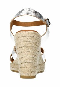Hakkensandaal met een gevlochten jute hak, zilveren metalen banden en een bruine leren enkelband. Gestructureerde hak en een glad voetbed.