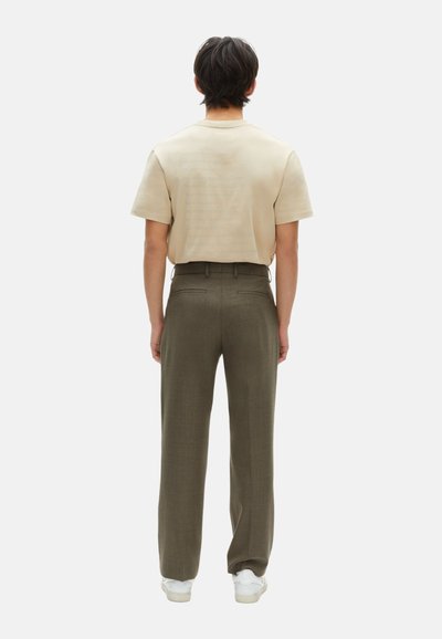 Camisa beige de manga corta con un sutil detalle de texto, combinada con pantalones de talle alto en verde oliva. El modelo lleva zapatillas blancas.