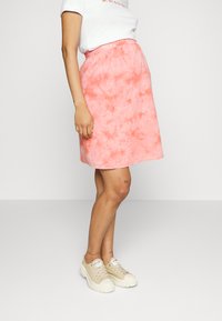 Saia em A com padrão tie-dye rosa, com cintura elástica, apresentando uma textura suave e um design até ao joelho, combinada com ténis bege.