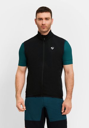 Mann trägt eine schwarze, ärmellose Weste mit Reißverschluss über einem türkisfarbenen Kurzarmshirt und dunkeltürkisen Shorts, steht vor einem schlichten weißen Hintergrund.