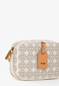 Borsa in tessuto con un'esterno a fantasia crema e oro. Presenta un'apertura con una finitura in pelle beige e un'etichetta per bagagli rettangolare.