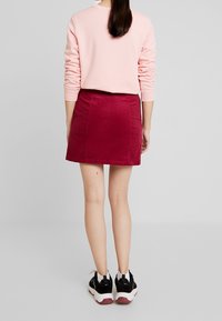 Růžová mikina s žebrovanými manžetami, doplněná o mini sukni z jemného manšestru v barvě mahagonu a černé sportovní tenisky s bílou podešví a červenými akcenty.