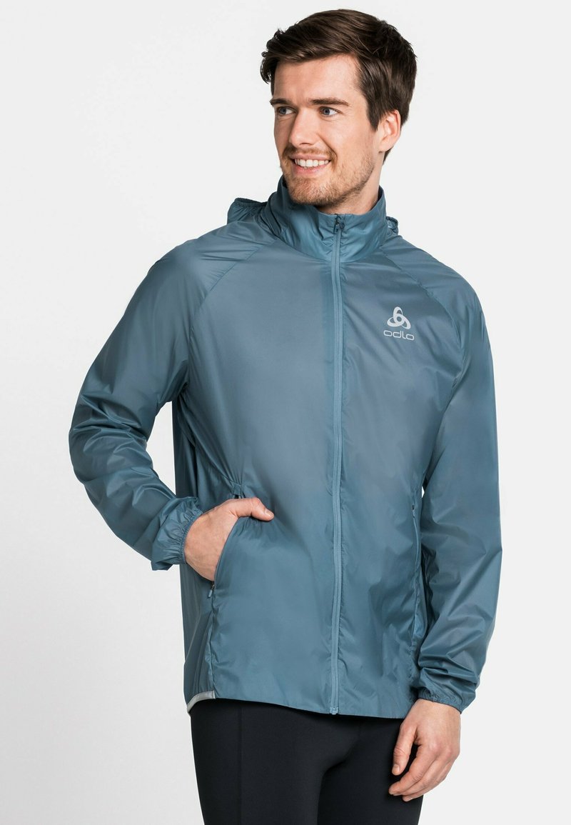 Lekki, niebieski wiatrówka z kapturem, długimi rękawami i elastycznymi mankietami; z przodu zapinana na zamek błyskawiczny oraz z bocznymi kieszeniami.