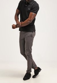 Mustapaita, jossa on pieni logo, harmaat slim-fit-housut ja mustat kengät. Rakenteellinen kangas, lyhyet hihat ja klassinen kaulus.