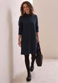 Robe pull bleu canard foncé à manches longues, motif texturé, col rond, associée à des leggings noirs et des bottes à lacets chunkys noires.