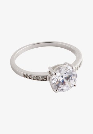 Silver ring with an oval clear stone, embellished with small diamonds along the band, set on a hand with a neutral-toned background.