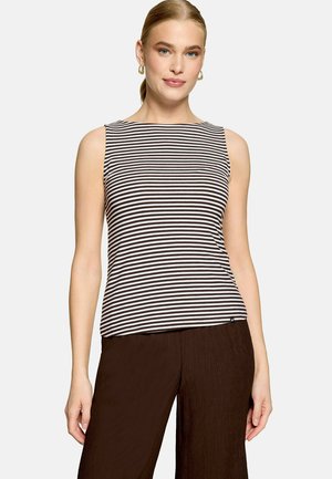 Femme en haut sans manches à rayures horizontales noires et blanches et pantalon ample marron foncé, cheveux attachés en arrière et boucles d'oreilles créoles dorées.