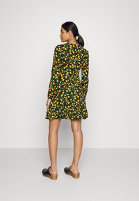 Vestido preto com um padrão de frutas laranja e folhas verdes. Mangas longas e bainha evasê; combinado com tamancos pretos de salto de madeira.