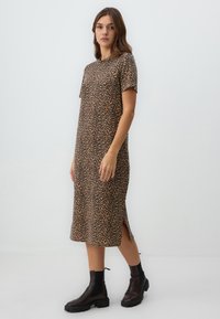 Leopardenmuster Kleid aus weichem Stoff, kurzärmelig, knielang, mit Seitenschlitzen, kombiniert mit schwarzen Knöchelstiefeln.