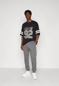 Czarny oversize t-shirt z grafiką "CHAMPION 92" i białymi paskami na rękawach; szare spodnie dresowe z bocznymi lampasami; białe trampki.